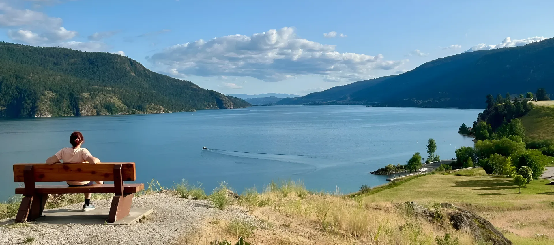 Une personne assise sur un banc devant un lac paisible entouré de montagnes