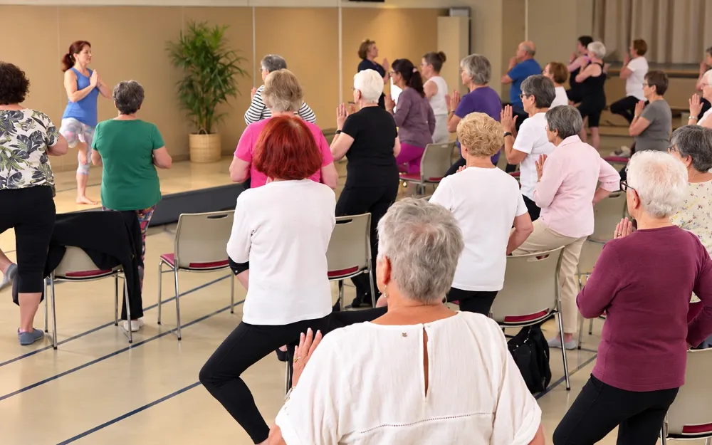 Cours de yoga en groupe au Centre : debout près de leur chaise, les participants tiennent la posture de l'arbre